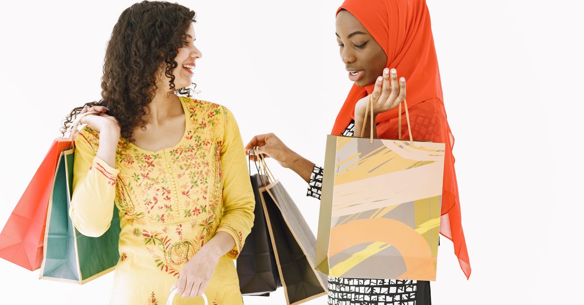 Two women in bright attire smiling and holding shopping bags against a white background.